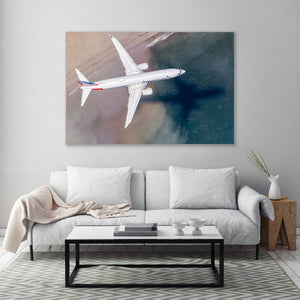 a large, white airplane flying over a beach, with a coffee table in the foreground.