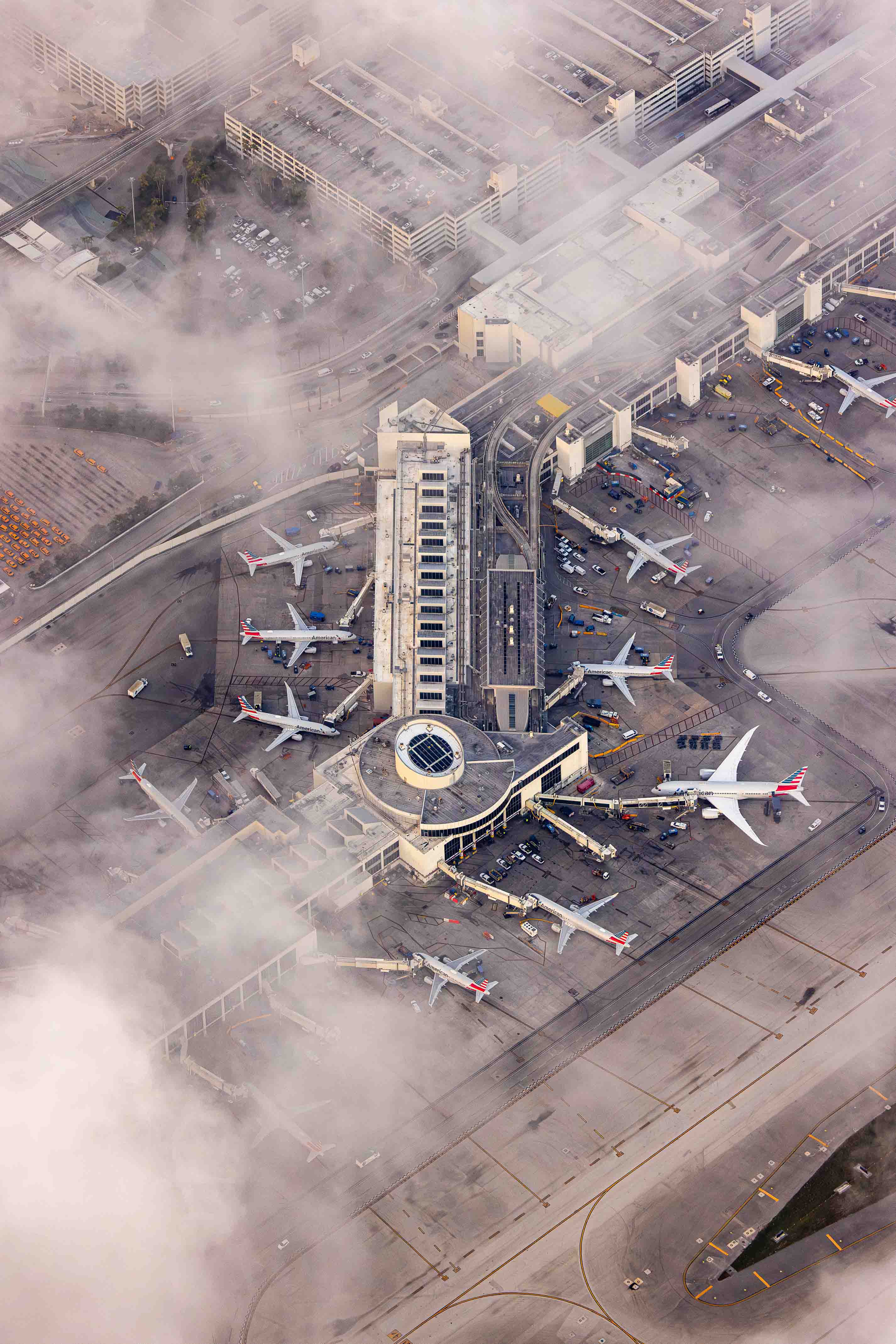 An aerial view of an airport with multiple airplanes parked at the terminals and a large building in the center.