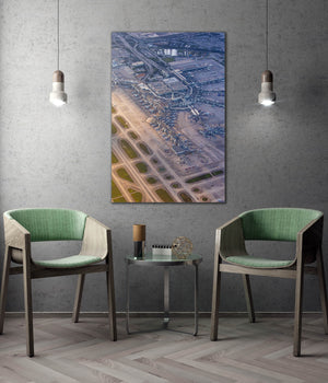 a modern living room with a large wall-mounted painting depicting an aerial view of an airport terminal and surrounding area. The room is furnished with two green chairs, and a small table is placed between them. The overall design and decor create a contemporary and stylish atmosphere.