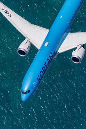 An aerial view of a large commercial airplane flying over a body of water, with the word "KOREAN" visible on the side of the aircraft.