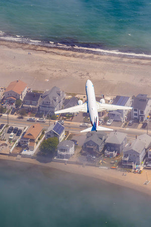 An aerial view of a large white airplane flying over a residential area with houses and cars on the ground.
