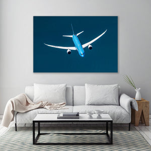 a large blue airplane flying in the sky, with a white couch and coffee table in the foreground.