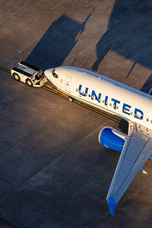 An aerial view of a United Airlines jet parked on the tarmac, with a service vehicle attached to the front of the aircraft.