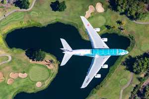 An aerial view of a large passenger jet flying over a golf course with a lake below.