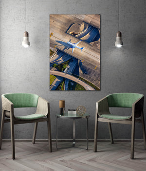 a modern living room with a large wall-mounted painting depicting an aerial view of an airport runway and tarmac. The room is furnished with two green chairs, and a small table is placed between them. The overall design and decor create a contemporary and stylish atmosphere.
