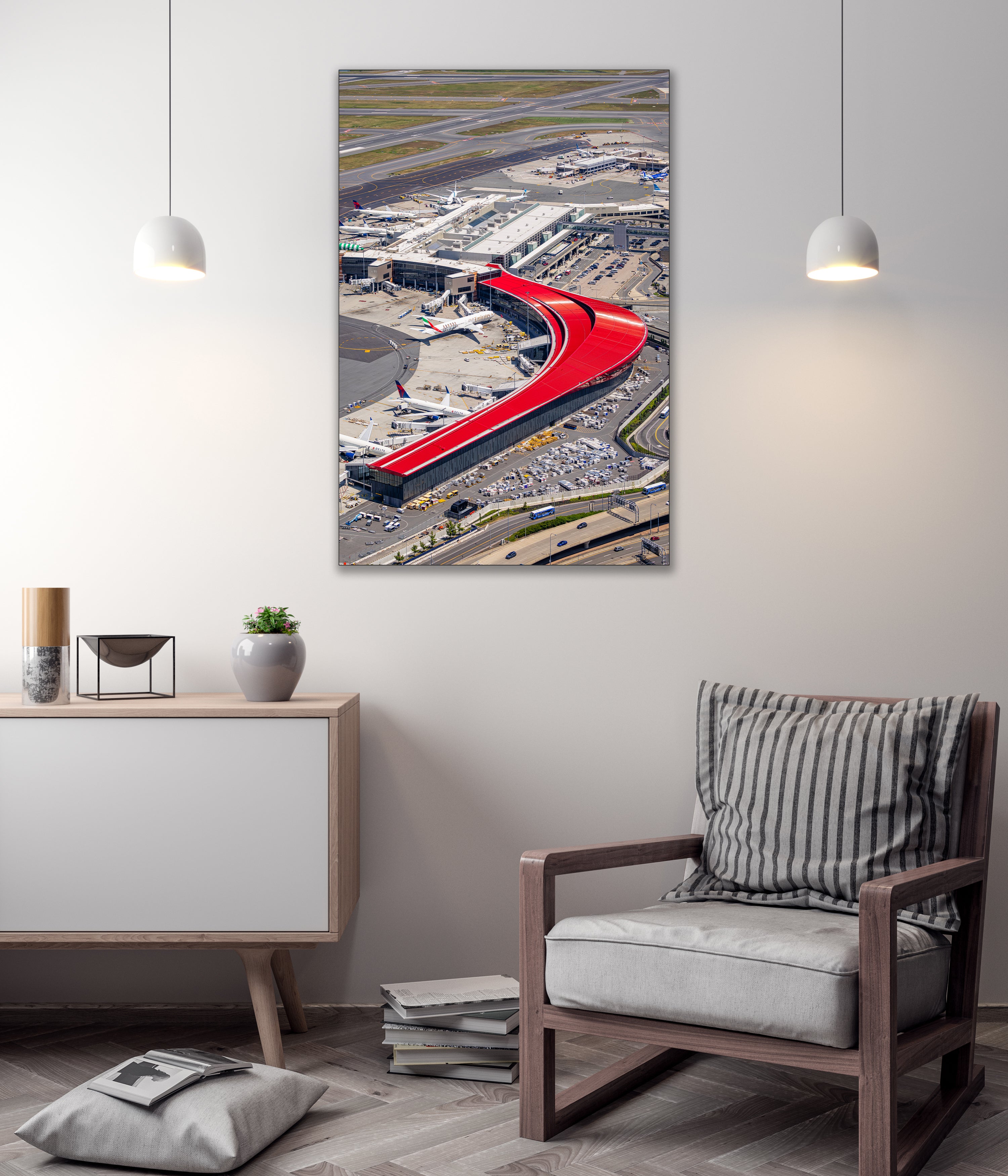 a modern living room with a large wall-mounted artwork depicting an airport terminal with a red curved structure. The room has a minimalist design, with a gray chair, a white cabinet, and a stack of books on the floor.