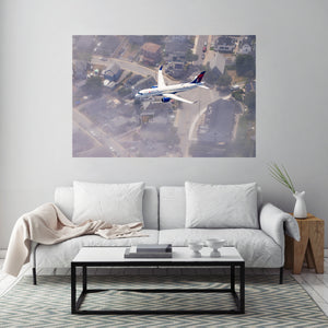 A large poster of an airplane flying over a residential area is displayed on the wall above a white sofa in a living room setting.