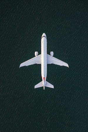 An aerial view of a large white airplane flying over a dark blue body of water.
