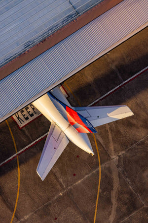 An aerial view of an airplane parked at an airport, with a building and a runway visible in the background.