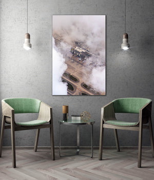 a modern living room with a large wall-mounted painting depicting an aerial view of a building shrouded in fog. The room is furnished with two green chairs, and a small table is situated between them. The overall design and decor create a contemporary and stylish atmosphere.