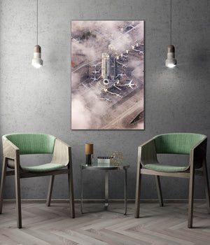 a modern living room with a large wall-mounted painting depicting an aerial view of an airport terminal surrounded by fog. The room is furnished with two green chairs, and a small table is placed between them. The overall design and decor create a contemporary and stylish atmosphere.