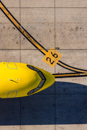 a yellow airplane parked on a concrete surface, with a yellow sign displaying the number "26" in the background.