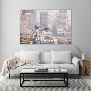 a large, colorful airplane flying over a cityscape, with tall buildings and a city skyline visible in the background.