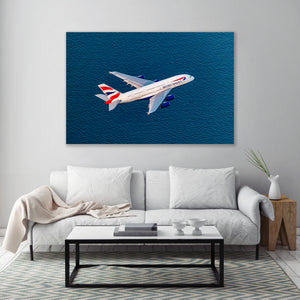 a large painting of a British Airways airplane flying over a body of water, mounted on a wall above a white sofa and a coffee table in a living room setting.