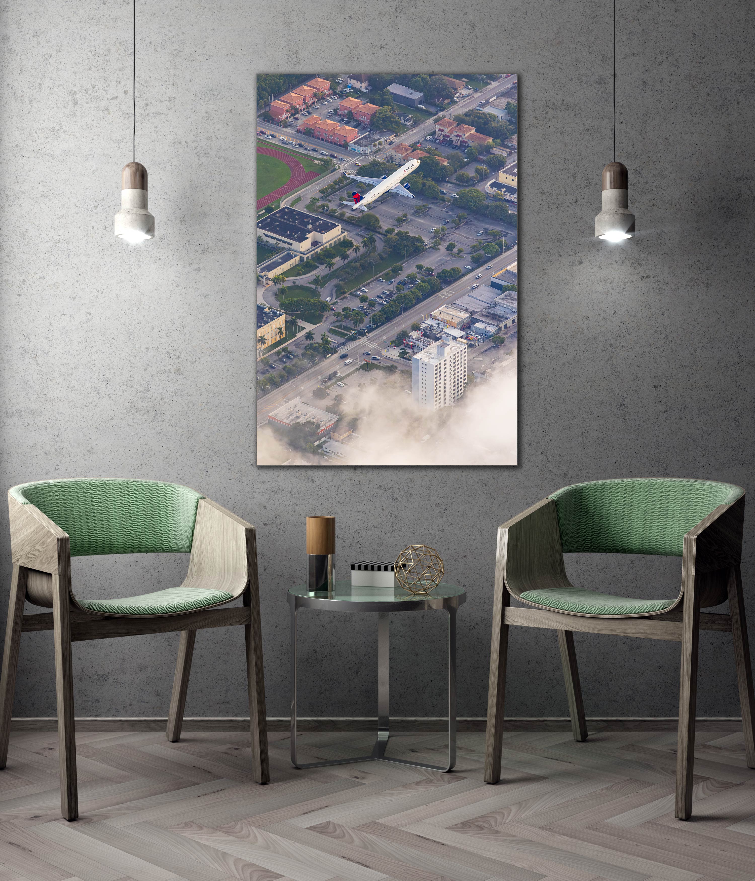 a modern living room with two green chairs, a glass coffee table, and a framed aerial view of a cityscape with a plane flying over it.