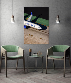 a large framed photograph of a United Airlines plane on the tarmac, with two green chairs positioned in front of it.