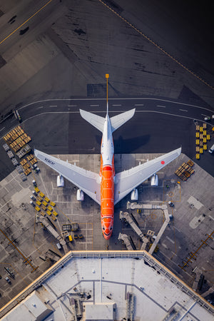 An aerial view of an orange and white airplane parked on the tarmac at an airport, with various ground support equipment and vehicles visible around it.