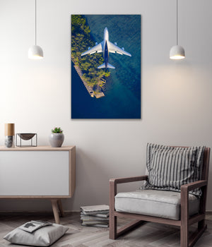 a large aerial view of a plane flying over a body of water, with a striped pillow on a chair in the foreground.