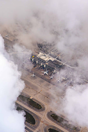 An aerial view of an airport with multiple airplanes parked on the tarmac, surrounded by clouds and fog.