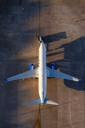 An aerial view of a large commercial airplane on a runway, with a person visible on the ground near the airplane.