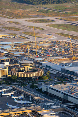 An aerial view of an airport with multiple buildings, cranes, and airplanes visible.