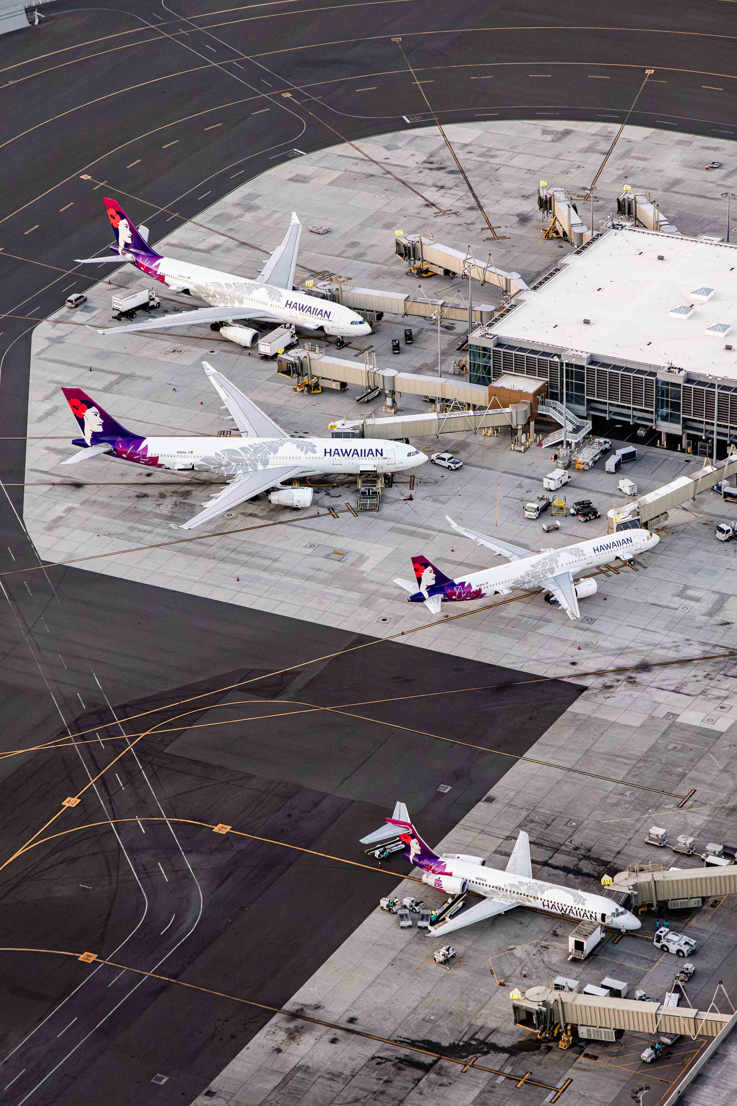 An aerial view of an airport tarmac with several commercial airplanes parked at the gates, connected to the terminal building.