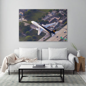 a large aerial view of a white airplane flying over a cityscape with buildings, trees, and roads.