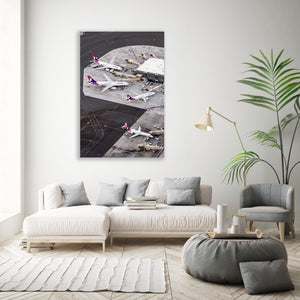 a large wall-mounted photograph of airplanes on an airport tarmac, with a white sofa, armchair, and potted plant in the foreground.