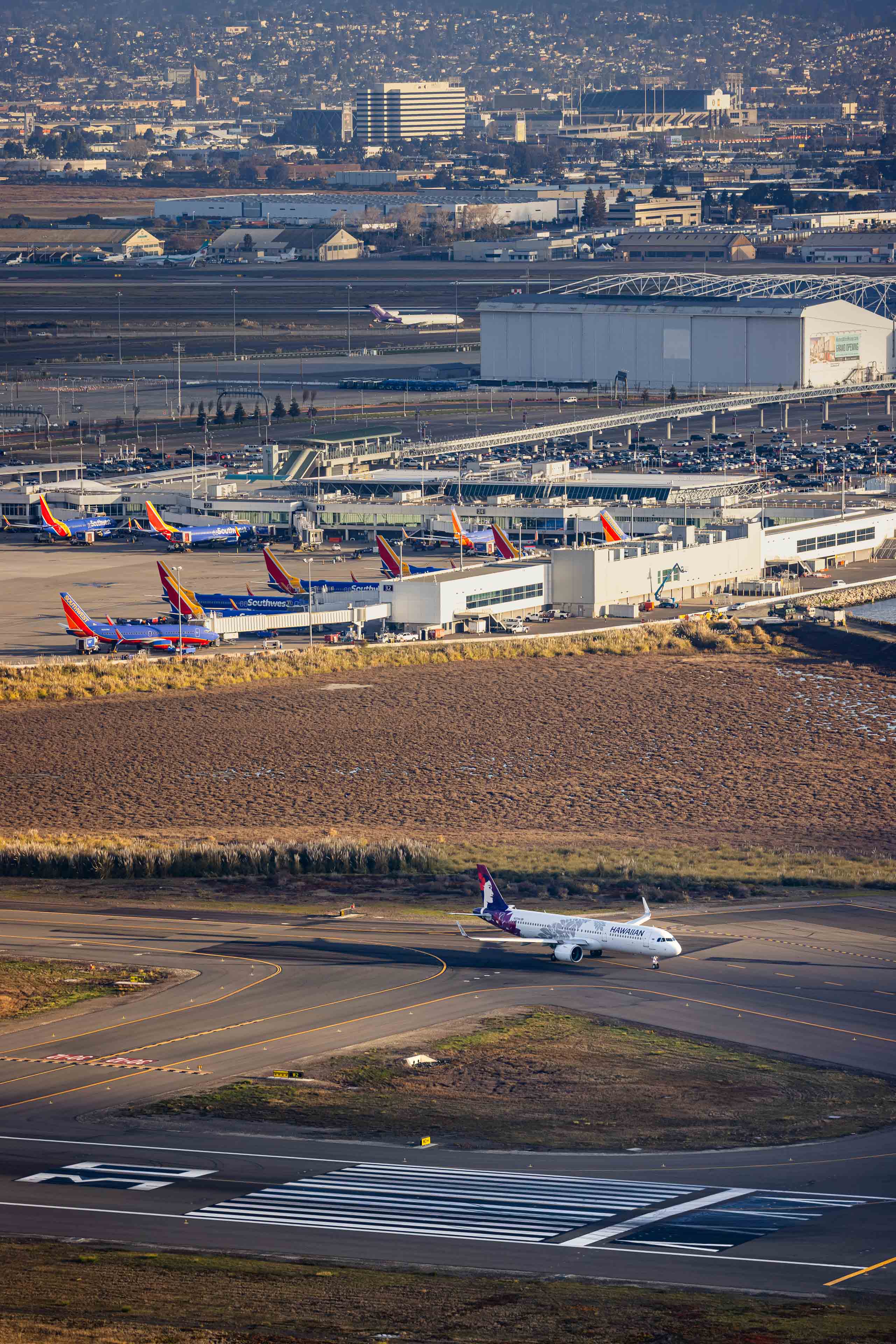 An aerial view of an airport with multiple airplanes parked on the tarmac, surrounded by buildings and a cityscape in the background.
