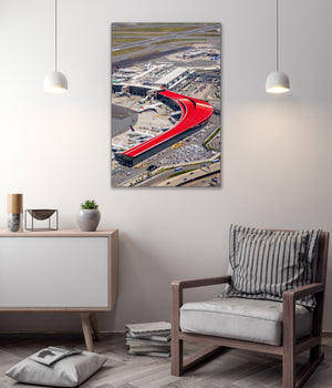 a modern living room with a large wall-mounted artwork depicting an airport terminal with a red curved structure. The room has a minimalist design, with a gray chair, a white cabinet, and a stack of books on the floor.