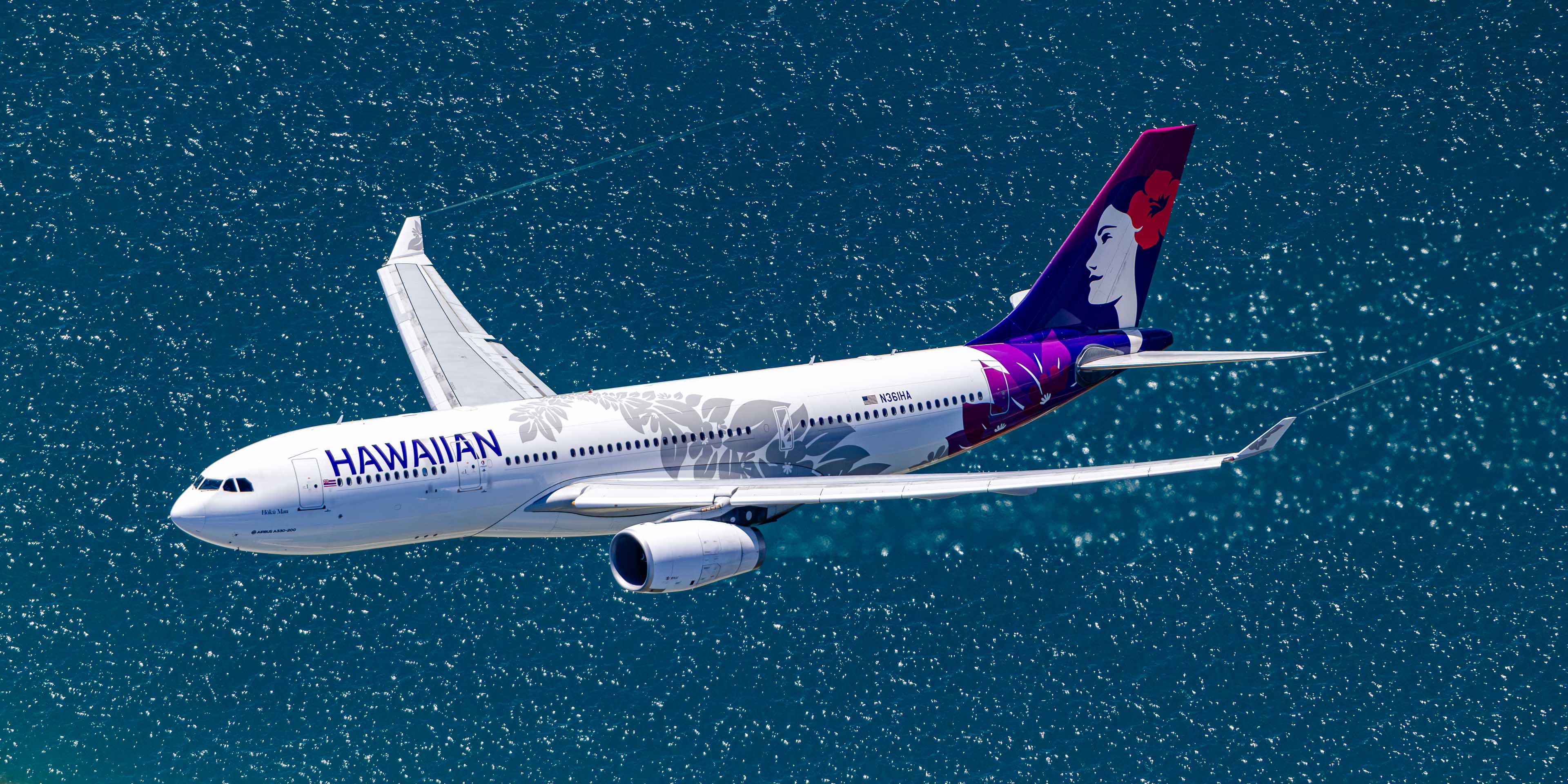 An aerial view of a Hawaiian Airlines passenger jet flying over a body of water.