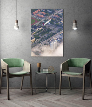 a modern living room with two green chairs, a glass coffee table, and a framed aerial view of a cityscape with a plane flying over it.