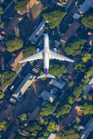 An aerial view of a large passenger jet flying over a residential area with houses and trees below.